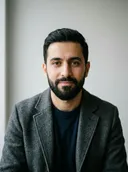 Photo de la personne transformée : un homme barbu en blazer gris et t-shirt noir devant un mur blanc